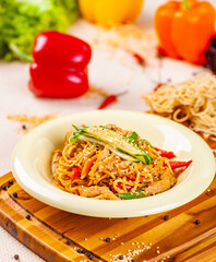 Noodles with vegetables and chicken in beige plate on wooden board