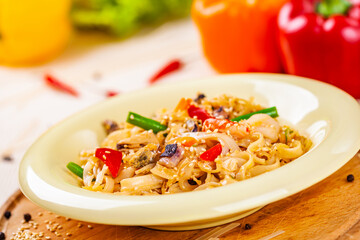 Pasta with seafood and vegetables in white plate on wooden cutting board