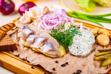 Appetizer. Herring, boiled potato, toasted bread, pickles, onion on wooden board
