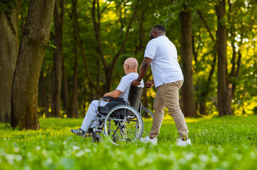 Caregiver and old man in a wheelchair. Professional nurse and patient walking outdoor in the park at sunset. Assistance, rehabilitation and health care.