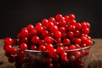 Ripe red viburnum in a dish on a wooden table. Medicinal plants. Dark background.