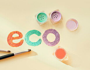 eco inscription made with mineral eyeshadows pigment in jars on yellow background. eco friendly cosmetic and make up.