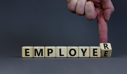 From an employee to an employer. Businessman turns a wooden cube and changes the word 'employee' to 'employer'. Beautiful grey background, copy space. Business, employee and employer concept.