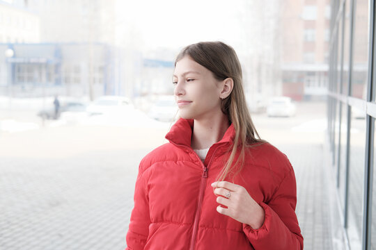 beautiful teenager girl wearing red jacket walking in the city enjoying nice weather in winter. teen girl looking aside and smiling