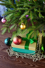 Fototapeta na wymiar Christmas gifts in beautiful package, in box with green ribbon and gold beads under Christmas tree decorated with balloons. Holiday gifts. Vertical photo. Close-up