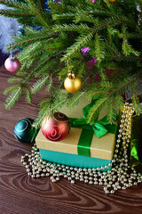 Christmas gifts in beautiful package, in box with green ribbon and gold beads under Christmas tree decorated with balloons. Holiday gifts. Vertical photo. Close-up