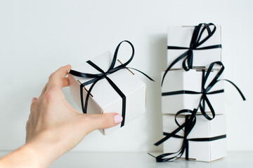 A female hand holds a small gift with a black ribbon on white background. Black Friday sale with stylish gift box present and black ribbon on white background. Black friday concept. 