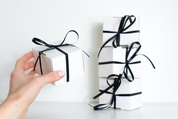 A female hand holds a small gift with a black ribbon on white background. Black Friday sale with...