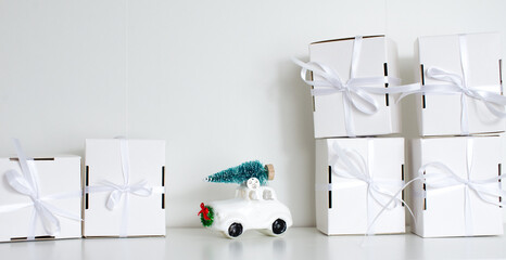 A small gifts and christmas ball car with a white ribbon on white background. Many white gifts with a bow. Christmas gifts. Gift for woman. Panorama christmas car with tree