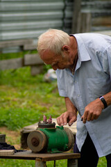 An elderly man, during repairs in the summer in the country, sharpens a knife on a grinding machine

