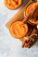 Organic pumpkin or sweet potato puree with cinnamon and anise star in glass jars, blue concrete background. Ingredient for making autumn or winter food.