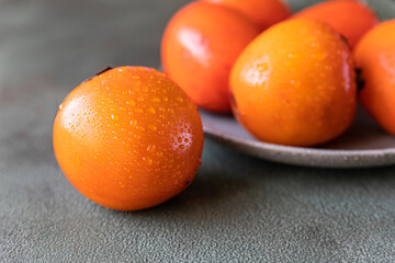 Ripe orange persimmon fruit with water drops on green concrete background.