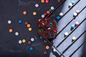 Chocolate muffin and lots of colored candies scattered about. Kitchen grate and cupcake. A ray of light from the window.