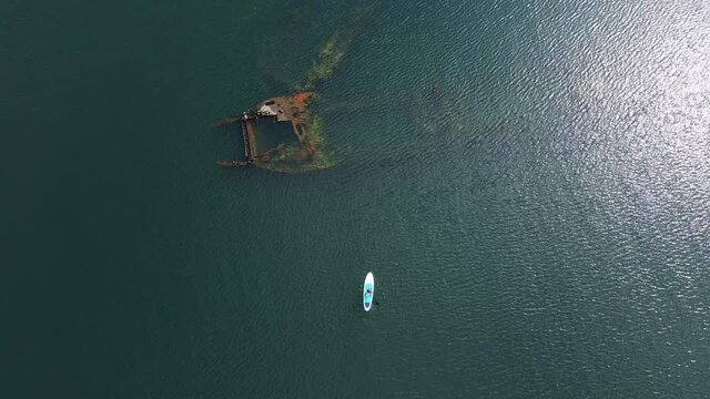 Aerial shot. Young women is having fun. Stand Up Paddling in the sea. SUP. Paddling among debrees of a sunk metal ships