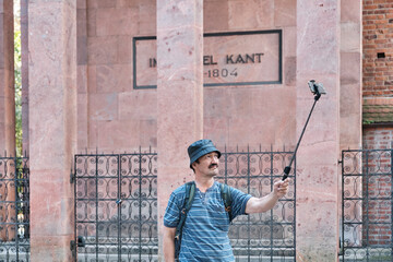 Senior Asian tourist with backpack taking selfie in front of grave of philosopher Immanuel Kant located on outside of Cathedral. - obrazy, fototapety, plakaty