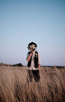 Wedding ceremony in rustic style, man in hat stay in a field and cover his face with flowers.