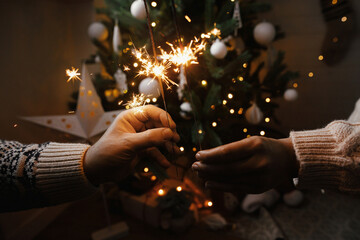 Couple hands with firework lights against christmas tree and glowing star. Happy New Year!