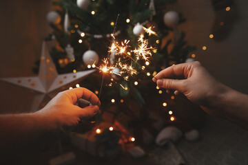 Fototapeta Happy New Year! Couple hands holding burning sparklers on background of christmas tree lights obraz