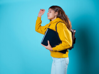Hurry up. A young woman with a laptop under her arm is running forward, a high pace of life. Student hurries to lecture, portrait in studio on blue