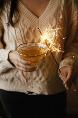 Happy New Year! Woman holding burning sparkler and champagne glass, celebrating New Year eve party