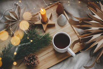 Atmospheric magic Christmas. Cup of tea, christmas stars, golden lights, trees, candle.Winter hygge