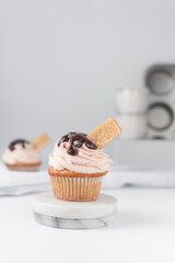 Vanilla cupcake with a tall swirl of pink frosting, chocolate glaze and a cookie, plain cupcake with pastel pink buttercream with chocolate and cookie garnish