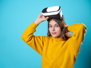 VR gamer, a young woman in a youth outfit uses a virtual reality helmet. A brunette in yellow on a blue background puts a vr gadget on her head