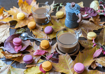 two cups of coffee, macaroons, coffee-pot and two tea spoons on the wooden table covered with fallen leaves