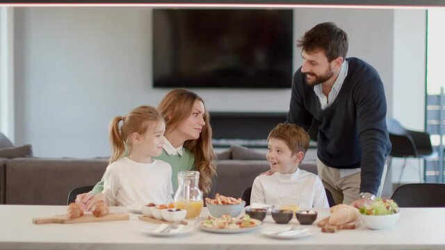 Young happy family talking while having breakfast at dining table at apartment