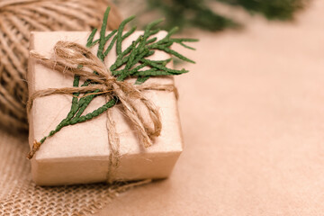 Festive decoration of gift in eco-style.Gift box is wrapped in craft paper,tied with cotton thread,decorated with thuja leaves and burlap.Christmas,New Year and eco-friendly concept.Copy space.