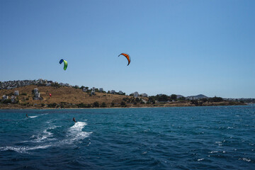 Two men are kite surfing in the Mediterranean sea against the backdrop of a peninsula with white houses, Bodrum, Turkey. Sports lifestyle concept. Kiteboarding or kitesurfing