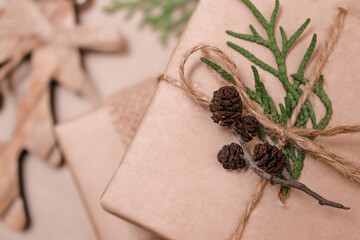 Festive decoration of gifts in eco-style.Gift boxes are wrapped in craft paper,tied with cotton thread,decorated with thuja leaves and cones,close-up.Christmas,New Year and eco-friendly concept.