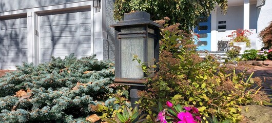 Fototapeta na wymiar A beautiful square lantern in a flowerbed with conifers and flowering plants. Garden design.