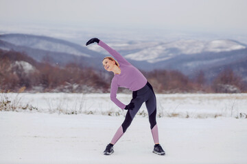 Slim sportswoman in shape doing warmup and stretching exercises in nature at snowy winter day....