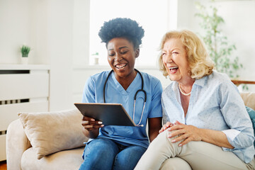 nurse doctor senior care tablet computer technology showing caregiver help assistence retirement home nursing elderly woman african american black happy laughing - Powered by Adobe