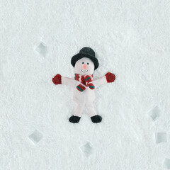 Snowman toy lying on snow. Pastel white natural abstract holidays background. Minimal flat lay. New year or christmas note card idea. Concept of winter leisure, recreation or children’s outdoor games.