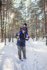 Fototapeta na wymiar Happy little boy sits on the shoulders of his father and wants to reach the branch and shake snow off the tree, active weekend, seasonal outdoor activities, family lifestyle, true moment