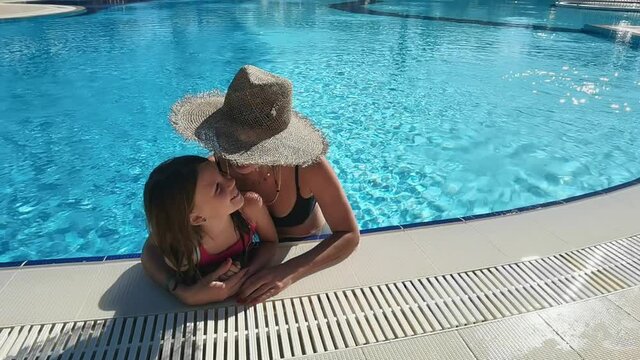 Young mother holding their cute child in their hands in the swimming pool and kissing him. Happy child is smiling.