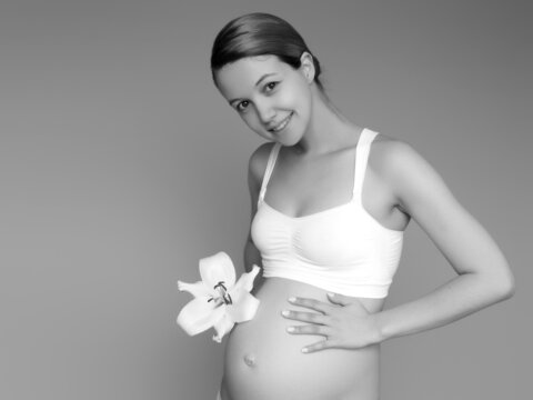 Beautiful pregnant young woman in clothes for pregnant women is measuring her bare tummy, smiling, on a background. Picture of happy pregnant woman posing over wall. Looking at camera