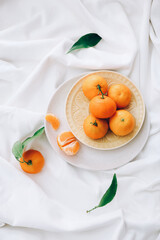 Fresh clementines with leaves on white fabric, top view