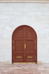 Closed wooden door with an arch in a stone white wall. Design and architecture