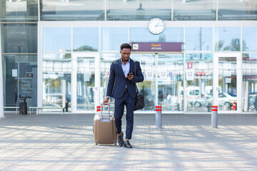 african businessman traveling near airport with suitcase calling taxi using mobile app
