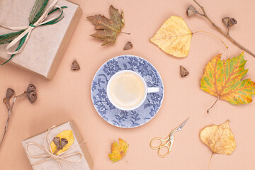 Fototapeta na wymiar Autumn composition. A cup of coffee in the center, yellow autumn leaves, a gift in craft paper and dried eucalyptus seeds on a beige background. Flat lay, top view, copy space