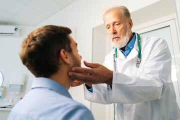 Close-up of mature adult male doctor otolaryngologist touching lymph nodes on neck and examining...