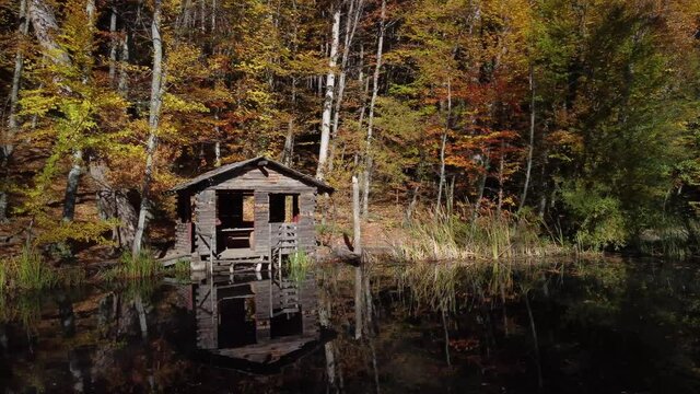 Fisherman's hut on the lake in the autumn forest. Bright foliage and smooth water surface. A cozy quiet place for meditation. The nature of the Crimea.