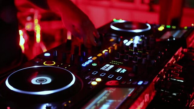 Party dj plays techno music on rave party in club. Disc jockey performing in nightclub. Disk jokey mixing musical tracks with audio mixer