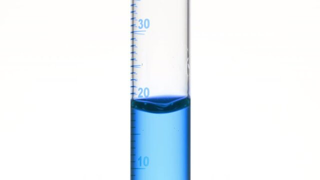 Drop of blue fluid is falling down into graduated cylinder with blue transparent fluid on white background | Abstract face care cosmetics formulation concept