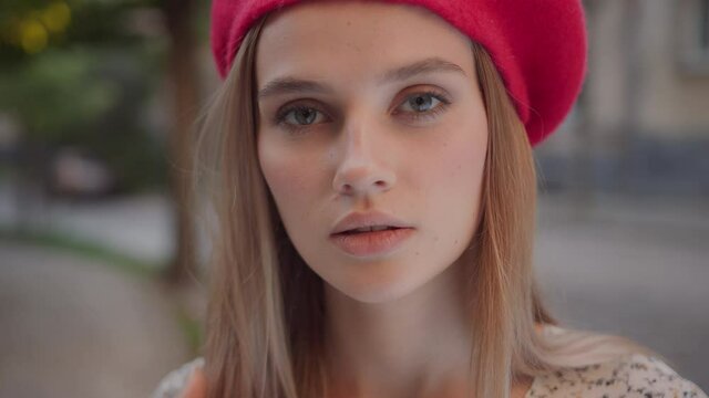 Closeup young caucasian woman in pretty stylish dress red beret outfit looking at camera standing on city street.