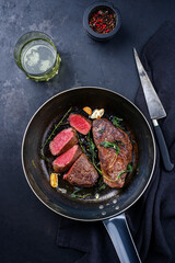 Traditional fried dry aged bison beef rump steaks with herbs and garlic served as top view in a...