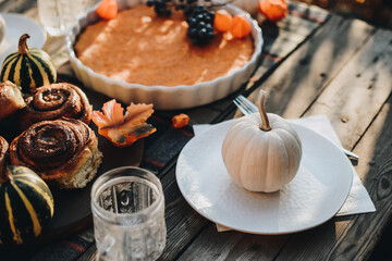 Thanksgiving festive table. Autumn style table setting with pumpkins, leaves and physalis. Pumpkin pie and cinnamon rolls. Cozy autumn scene. Flat lay. Fall styled composition.